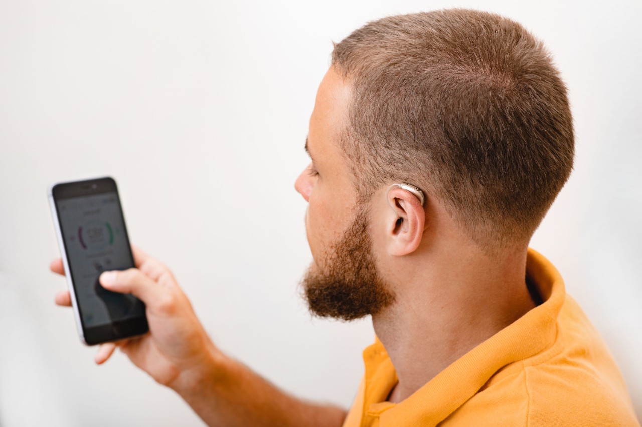 A man adjusting settings for his hearing aid via smartphone