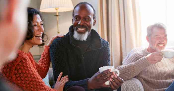 Man holding a cup of coffee conversing and smiling with friends