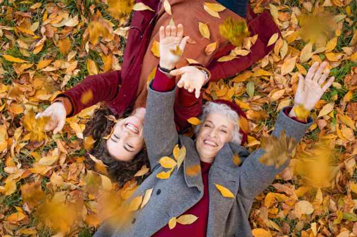 Two women smiling and laying in a pile of falling autumn leaves