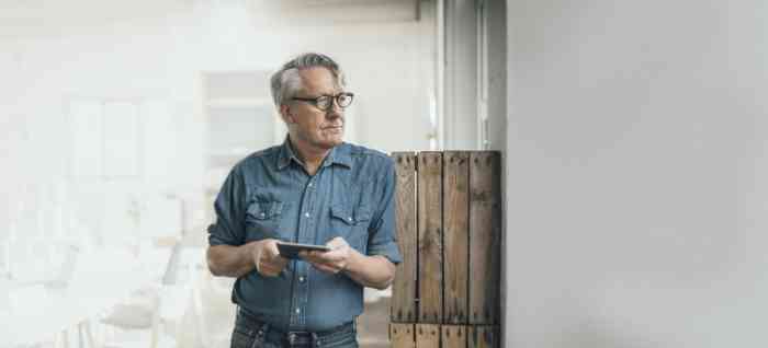 Elderly man with glasses holding a tablet in his hands