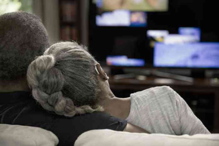 An elderly couple with BTE hearing aid watches TV on a sofa