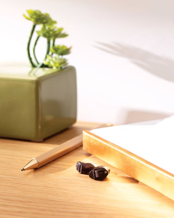 Small hearing aid on a table next to a pencil