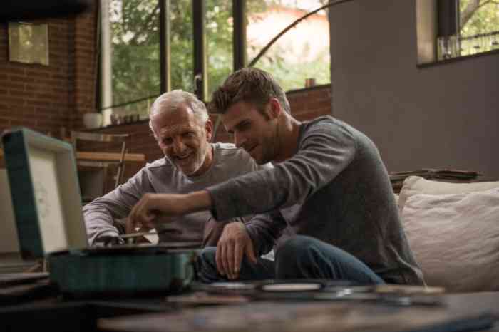 Older man and his adult son laughing and playing with a record player 