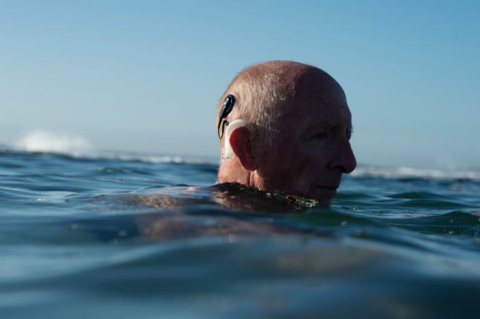 Old man swimming with covered hearing aid