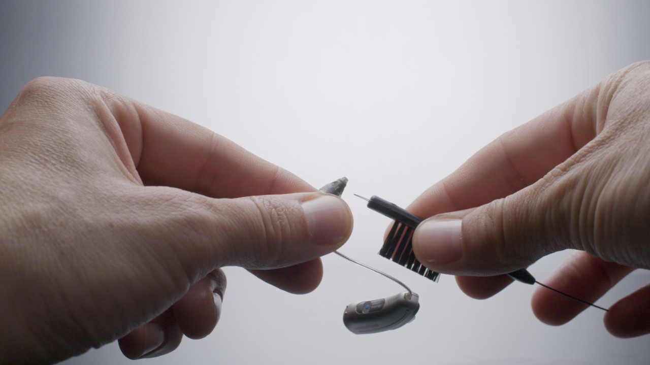 Cleaning hearing aid using a brush